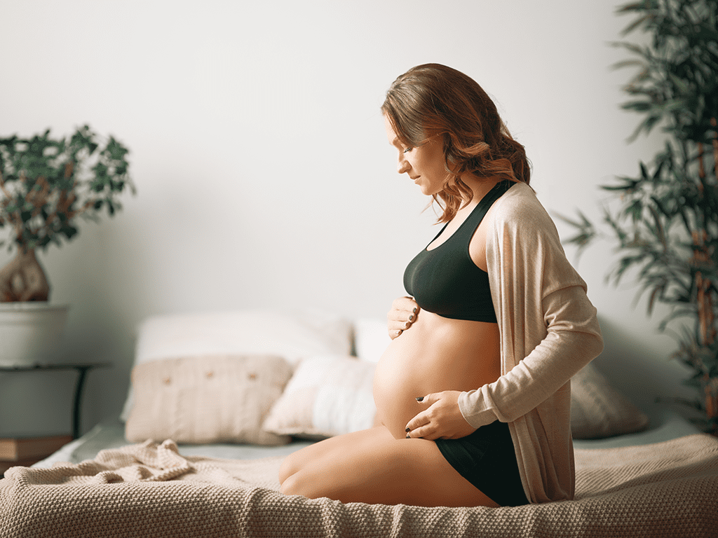 A pregnant woman sitting on the bed in her underwear.