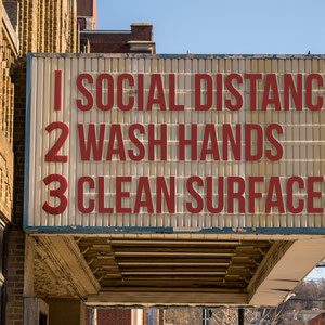 A sign on the side of a building that says social distance, wash hands and clean surface.