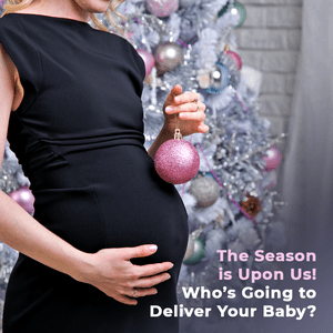 A pregnant woman holding a pink ornament in front of a christmas tree.