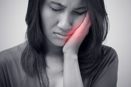 A woman holding her face in pain with red light coming from behind it.