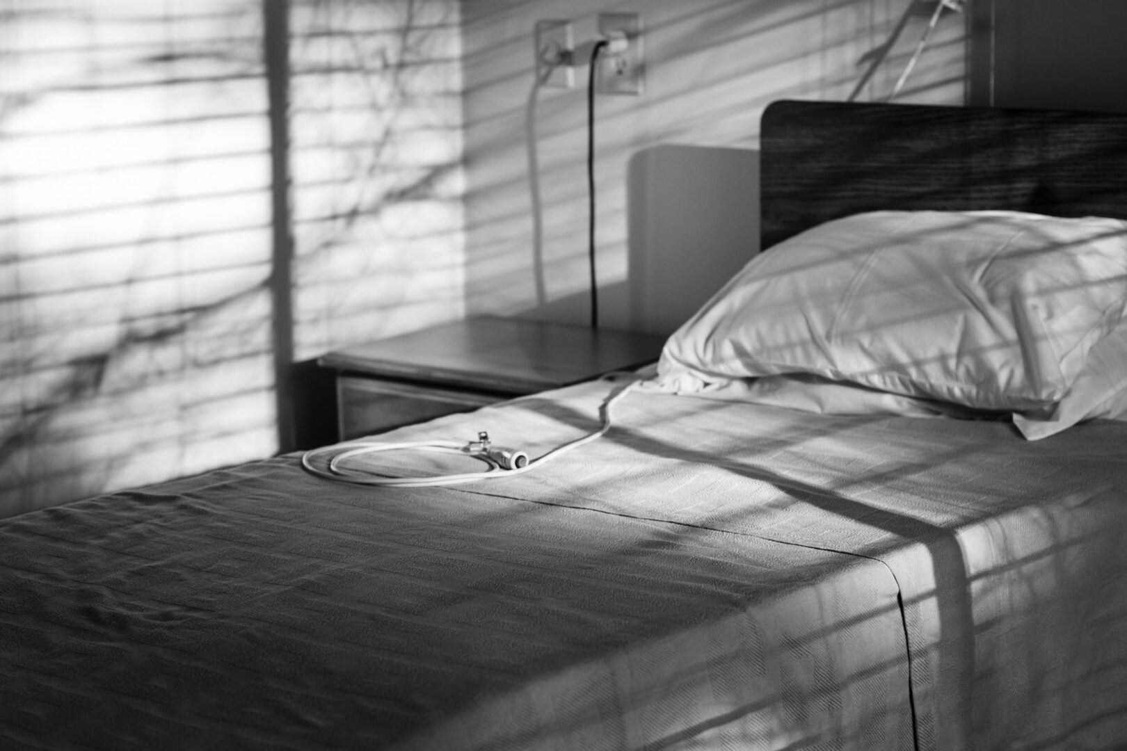 A bed with white sheets and pillows in the sunlight.