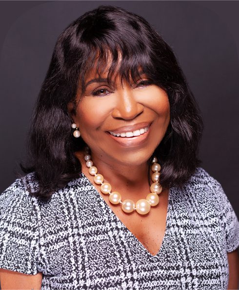 A woman with long black hair wearing pearls.